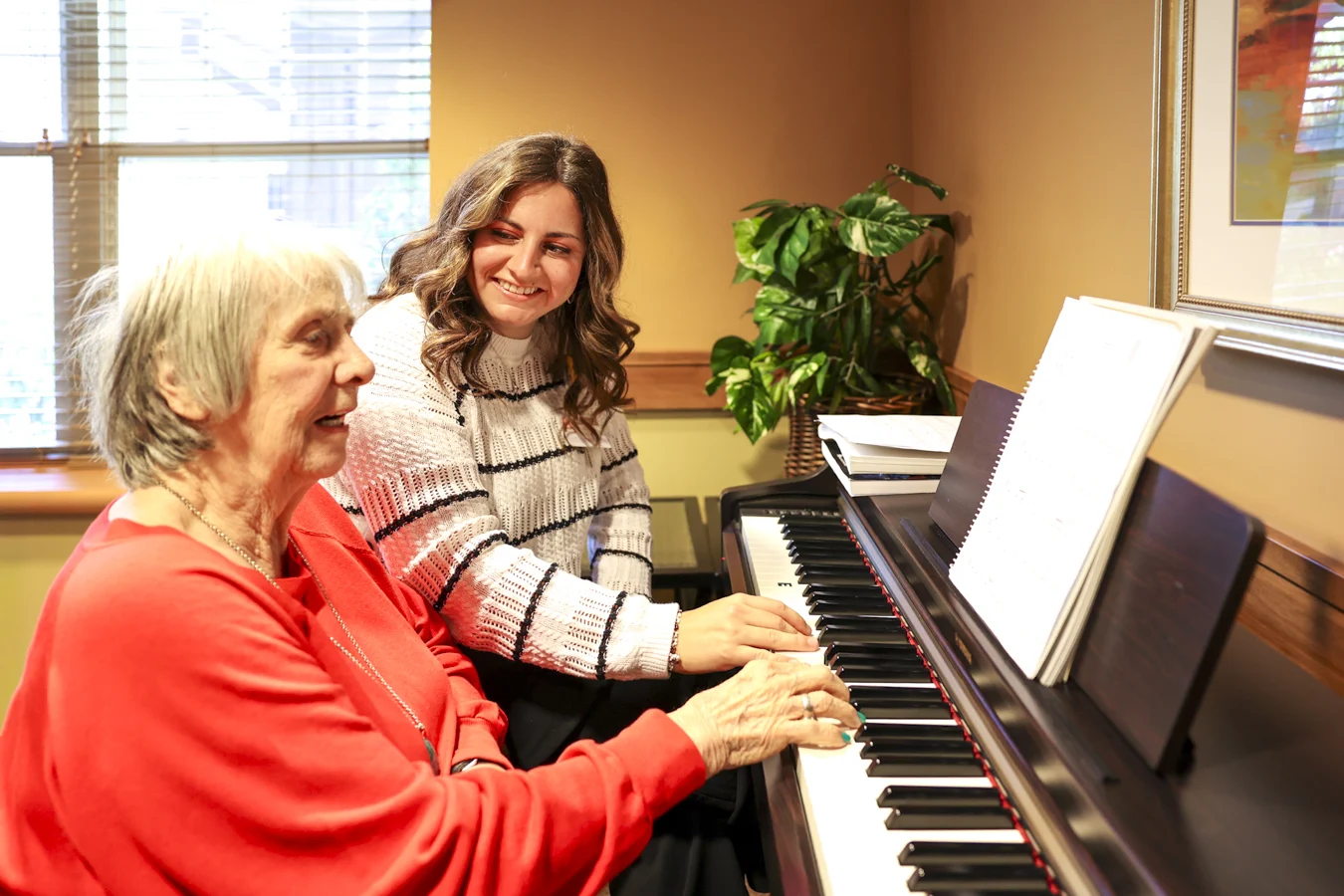 1W8A4157 Senior woman playing piano along with younger woman behind her.