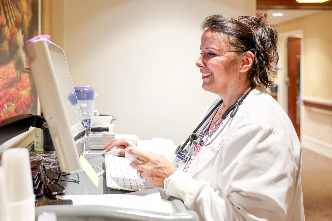 Smiling nurse with a stethoscope around her neck working at a computer station.
