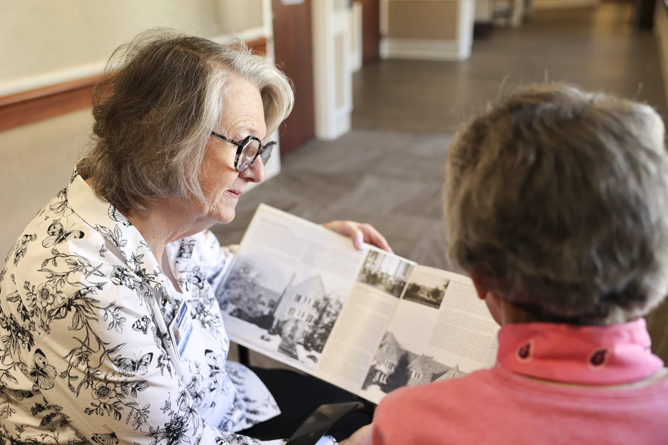 1W8A8424 Hospice volunteer reading book to woman seated next to her.