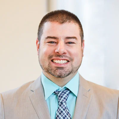 2V9A0358-Edit Smiling man in suit and tie standing indoors.