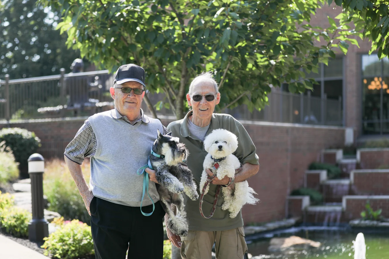 2V9A1410 Smiling senior men holding their dogs while standing outdoors together.