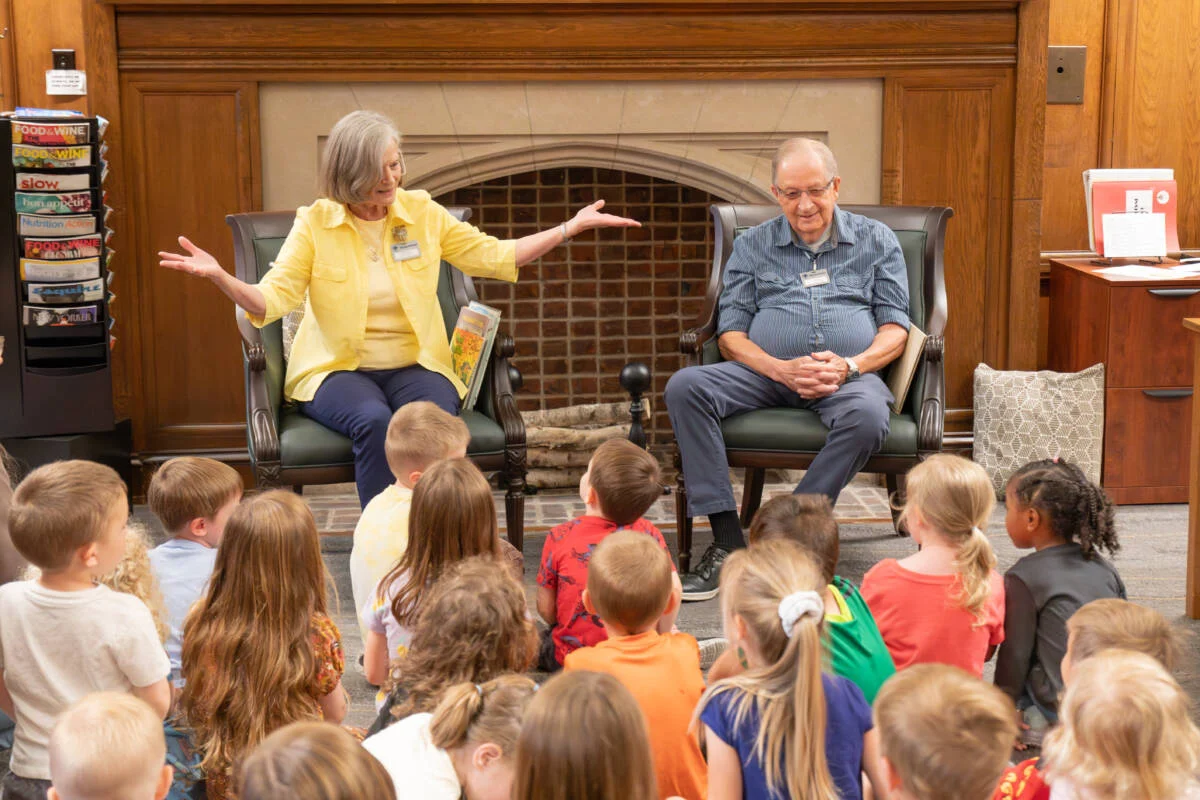 Two smiling senior volunteers talking to a group of young children.