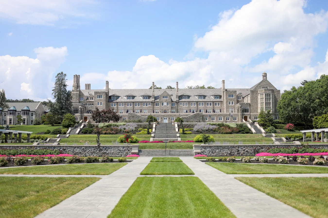 Large stone building with staircases leading down to well-manicured gardens.