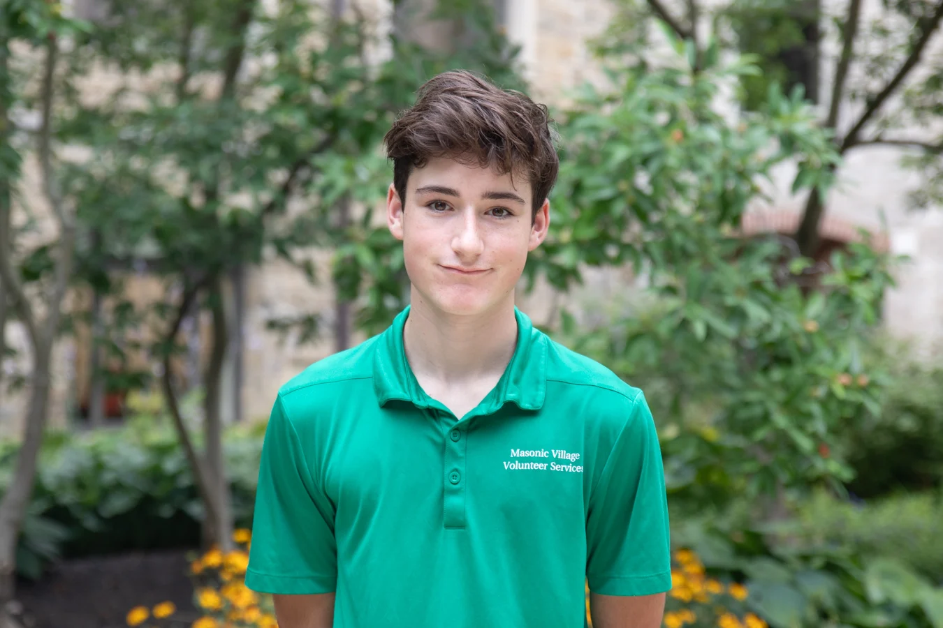 2V9A5517 Smiling young man wearing a green Masonic Village Volunteer Services shirt while standing outdoors.