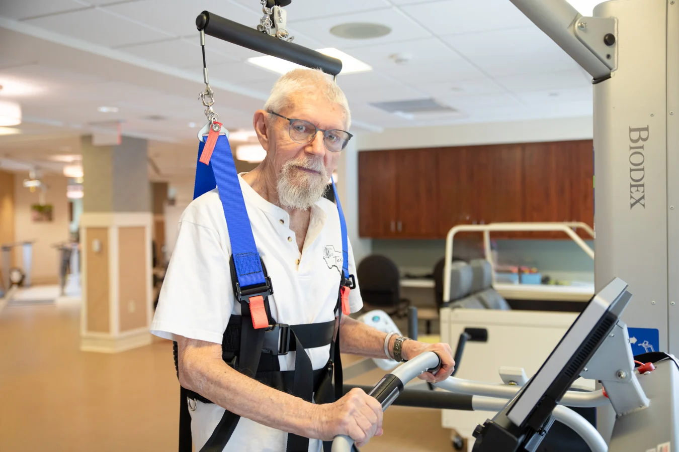 Senior man using a harness and a machine while in a rehabilitation center.