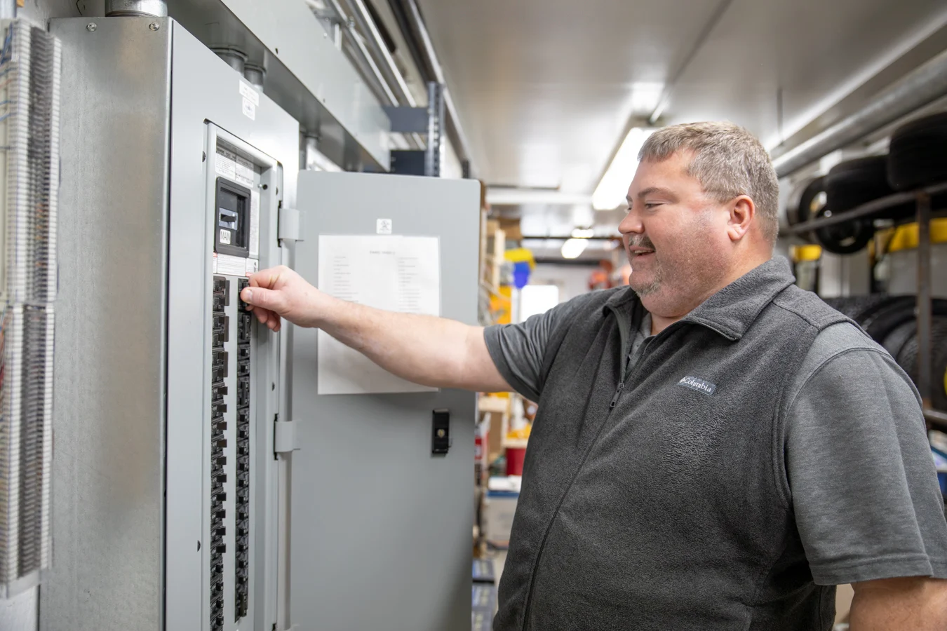 Smiling man working on a breaker box in a large utility room.