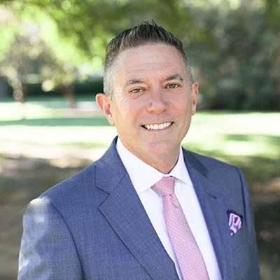 2V9A9224 Smiling man with short hair, wearing a suit and tie while standing outdoors.