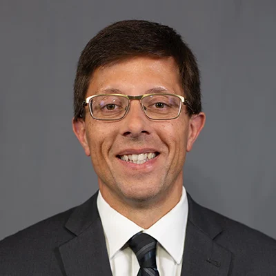 858A7049 Smiling man with glasses in a suit and tie.