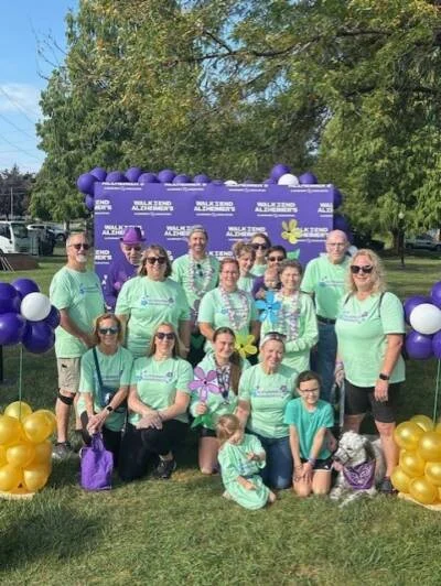 Smiling group dressed in green posed in front of a purple backdrop outdoors.
