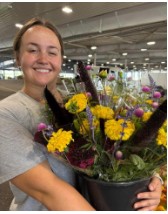 Young woman smiling while holding up a pot of flowers.