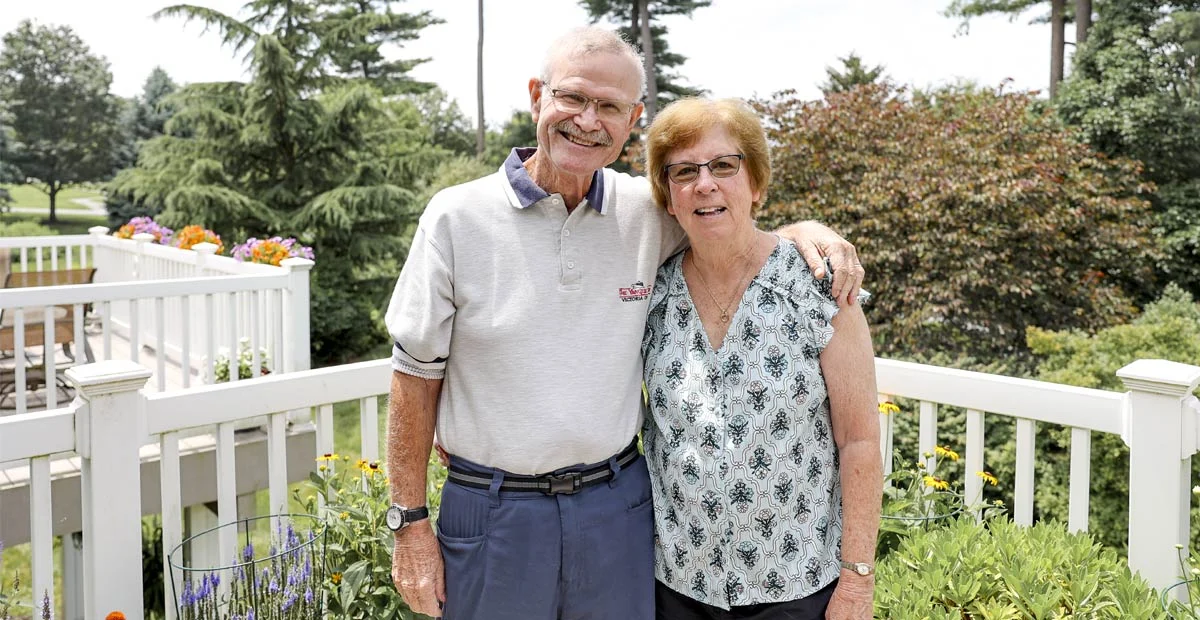 Dunlaps Smiling senior couple standing together on their balcony.