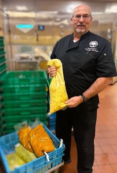Smiling man in a kitchen holding up bags of soup.