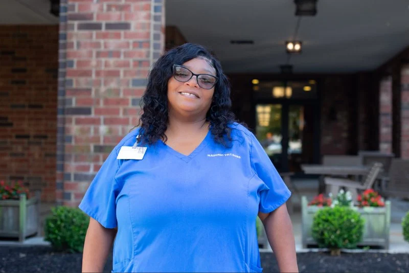 Smiling nurse standing outdoors in front of a building entrance.