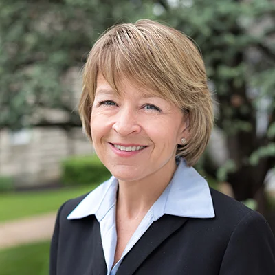 PamFormica Smiling woman with short hair wearing a blazer while standing outdoors.