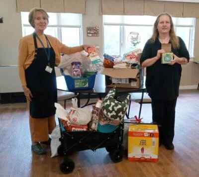 Two women standing on either side of boxesand a wagon filled with donations.