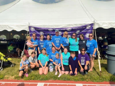 Smiling group posted in front of a Relay for Life banner and tent.