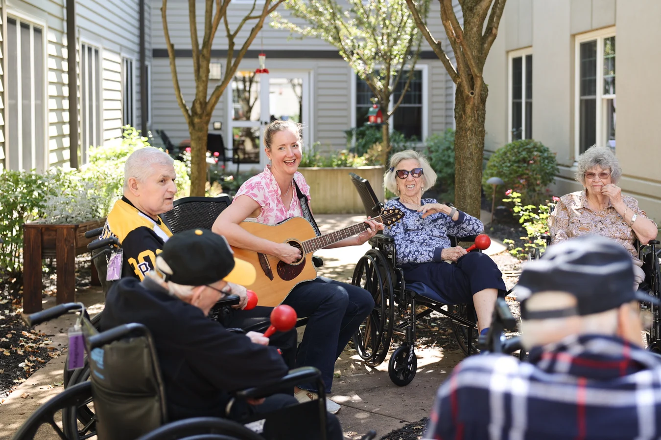 Smiling woman strumming a guitar surrounded by seniors outdoors.