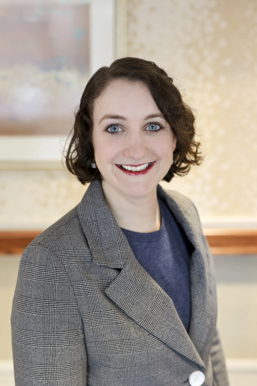 Smiling woman with short brown hair wearing a blazer and standing indoors.