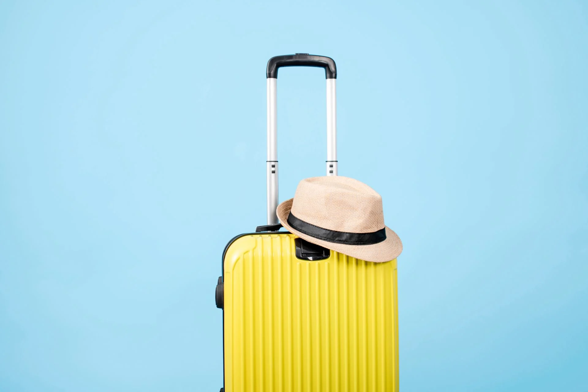 Yellow suitcase with a hat against a bright blue background.